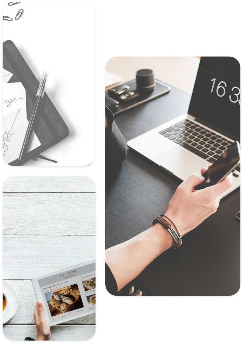 a pen and papers over a diary, a tablet displaying gourmet food and a hand holding a phone in front of a laptop over a table