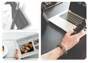 a pen and papers over a diary, a tablet displaying gourmet food and a hand holding a phone in front of a laptop over a table