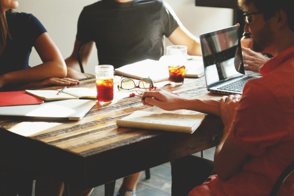 people huddles around a table with stationery, drinks and devices