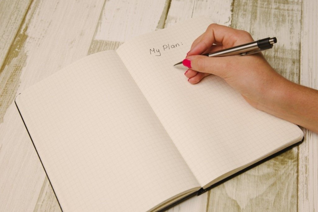 a person's hands taking notes in a diary over a table representing the planning stage in software testing